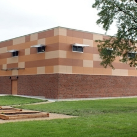 Modern two-story school building with brick lower level and tan and orange upper level. Raised garden beds in foreground.